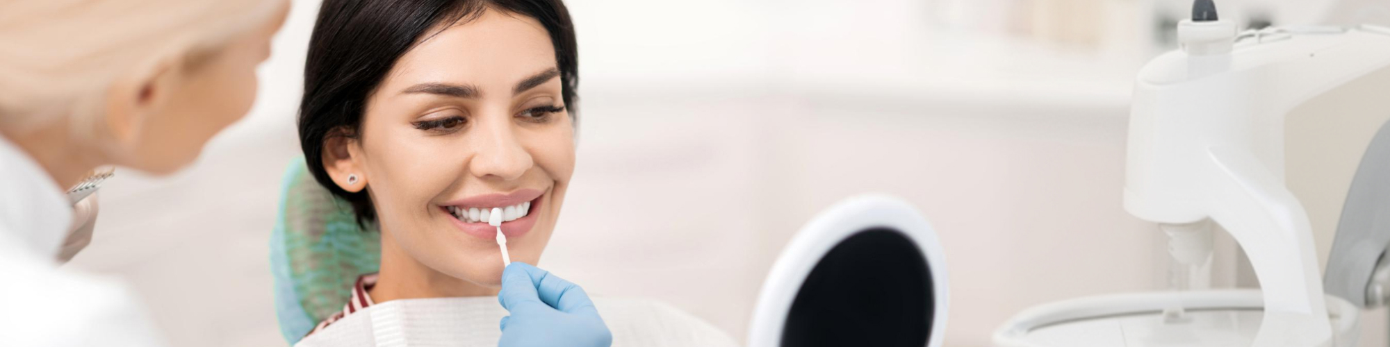 Gloved hand holding tooth shade-matching tool against woman's smile.